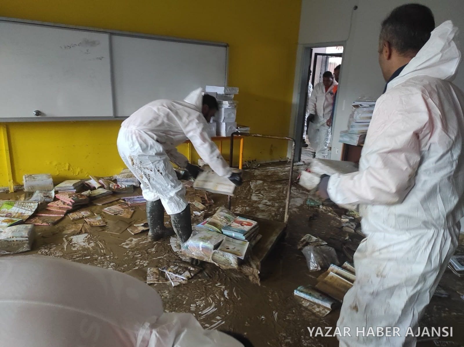 Koruyucu tulum giymiş ekipler, sel suyunun çamurla doldurduğu bir sınıfta ıslanan kitapları topluyor (Fotoğraf: İstanbul Büyükşehir Belediyesi AKOM)