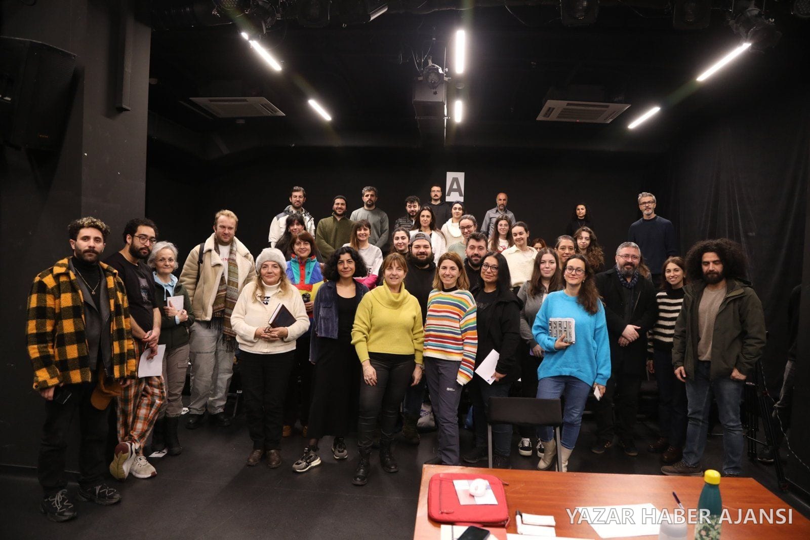 Çağdaş Oyun Yazım Atölyesi katılımcıları ve eğitmenleri bir stüdyo sahnesinde toplu fotoğraf çektiriyor (Fotoğraf: İBB Şehir Tiyatroları)